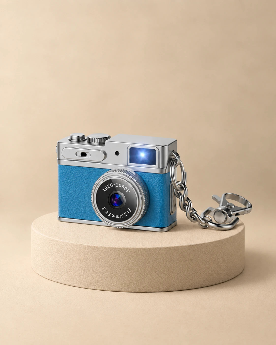 Mini appareil photo rétro bleu avec sa chaîne porte-clés, posé sur un socle beige