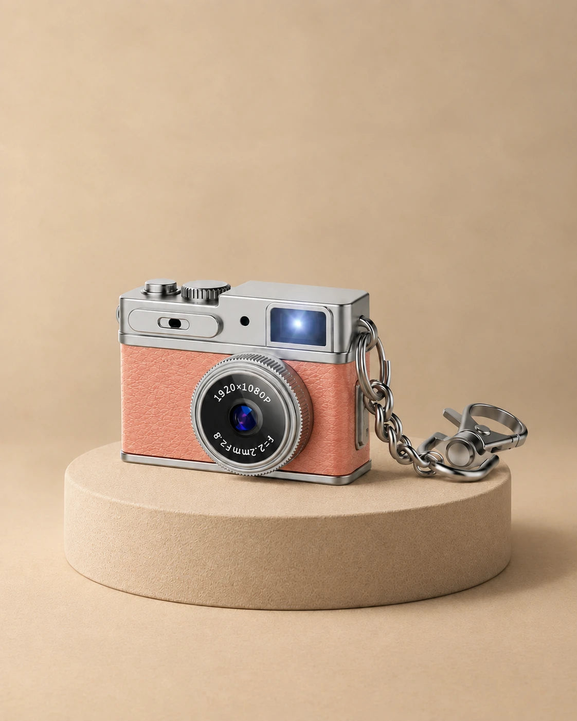 Mini appareil photo rétro rose avec sa chaîne porte-clés, posé sur un socle beige