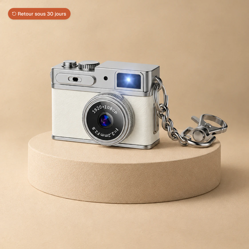 Mini appareil photo rétro blanc avec sa chaîne porte-clés, posé sur un socle beige