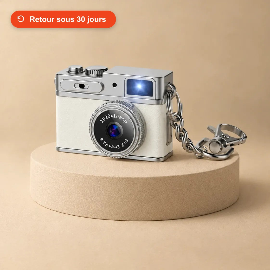 Mini appareil photo rétro blanc avec sa chaîne porte-clés, posé sur un socle beige
