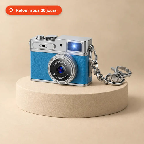 Mini appareil photo rétro bleu avec sa chaîne porte-clés, posé sur un socle beige
