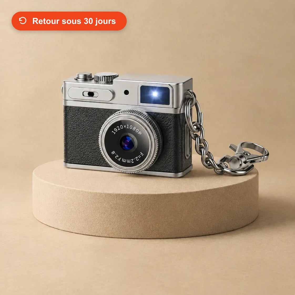 Mini appareil photo rétro noir avec sa chaîne porte-clés, posé sur un socle beige