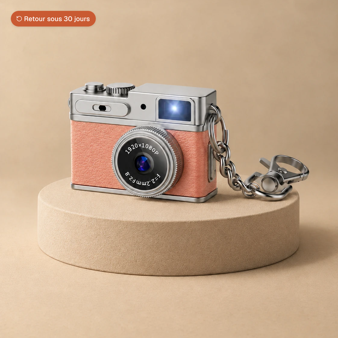 Mini appareil photo rétro rose avec sa chaîne porte-clés, posé sur un socle beige