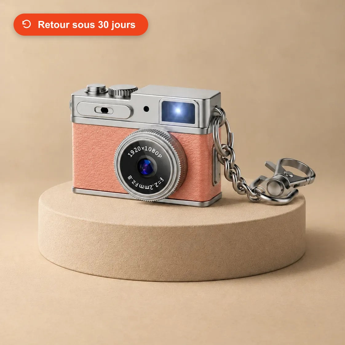 Mini appareil photo rétro rose avec sa chaîne porte-clés, posé sur un socle beige