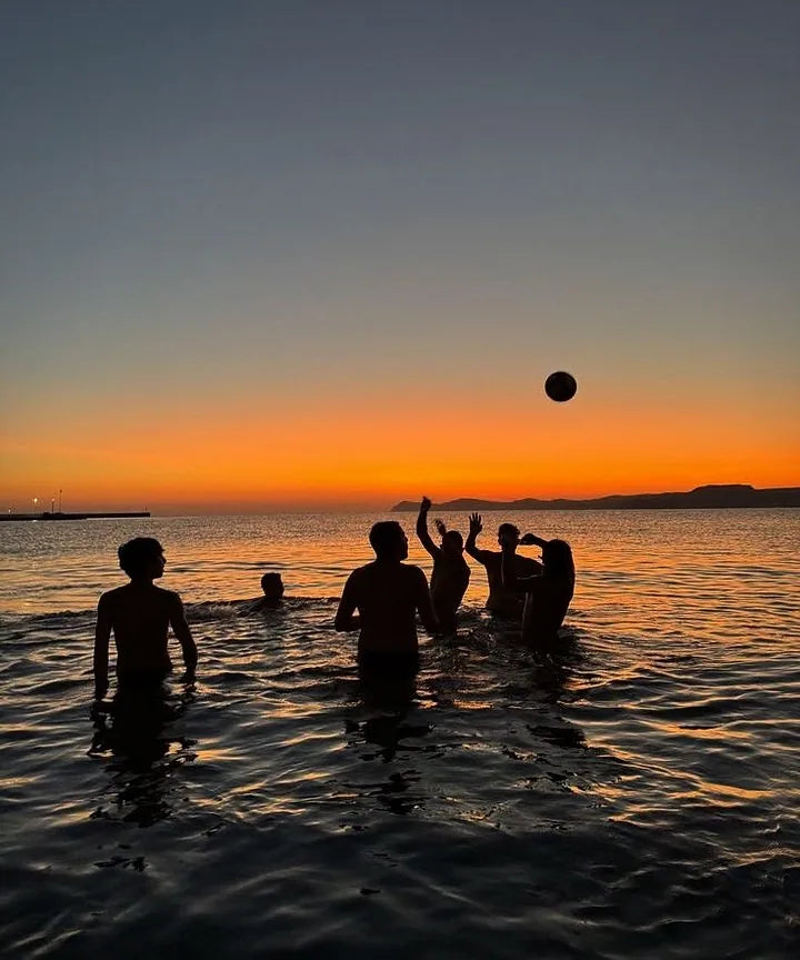 Silhouettes de personnes qui jouent au ballon dans la mer au coucher du soleil
