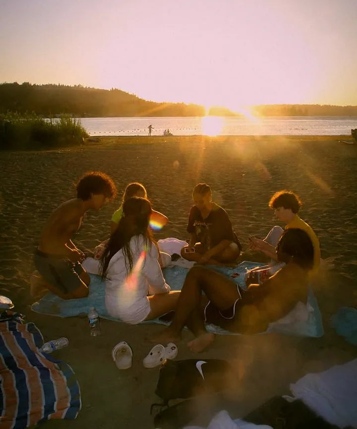 Groupe de jeunes assis sur une serviette de plage au coucher du soleil