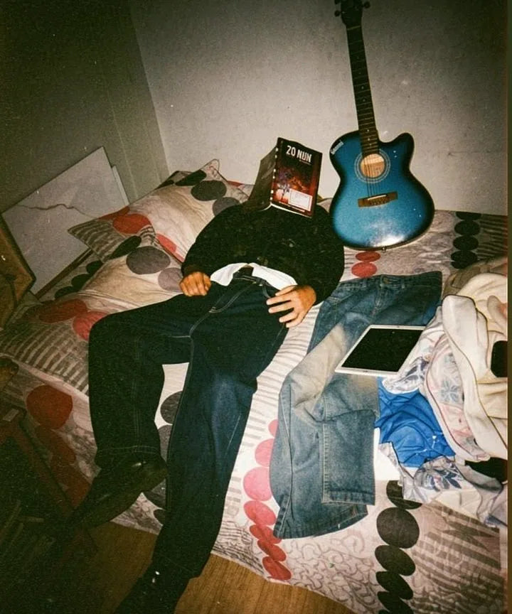 Garçon allongé sur un lit, un livre sur le visage, une guitare derrière lui