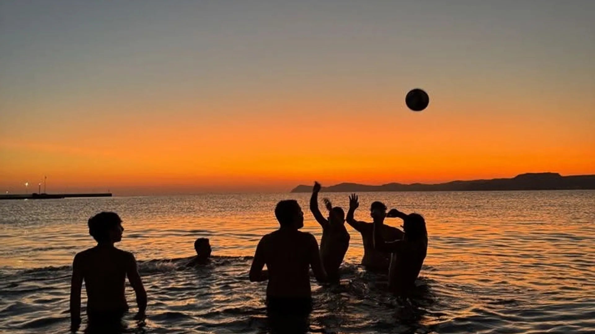 Silhouettes de personnes qui jouent au ballon dans la mer au coucher du soleil